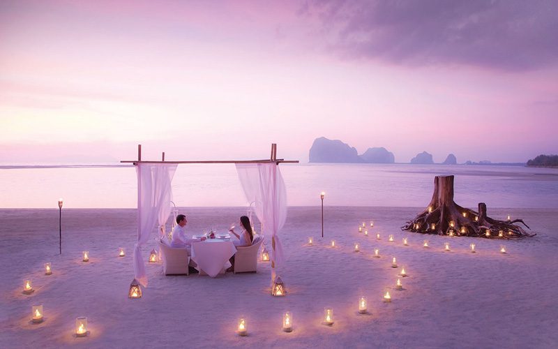 A young couple, enjoying a romantic, candlelit dinner, by the beach