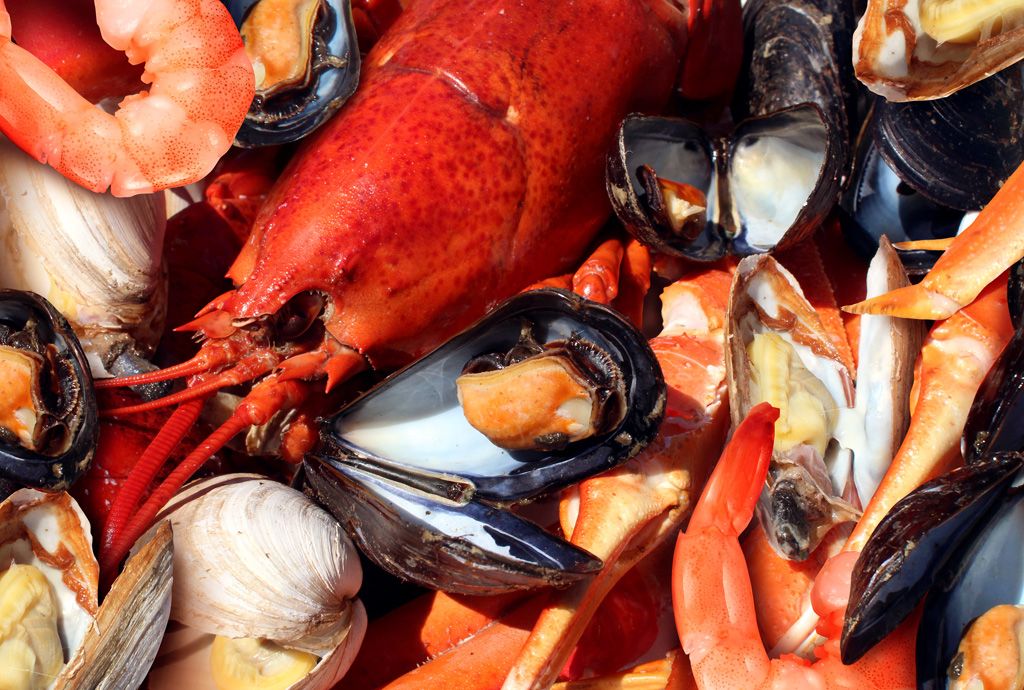 A basket filled with lobsters, shrimps, oysters, crab legs and clams.